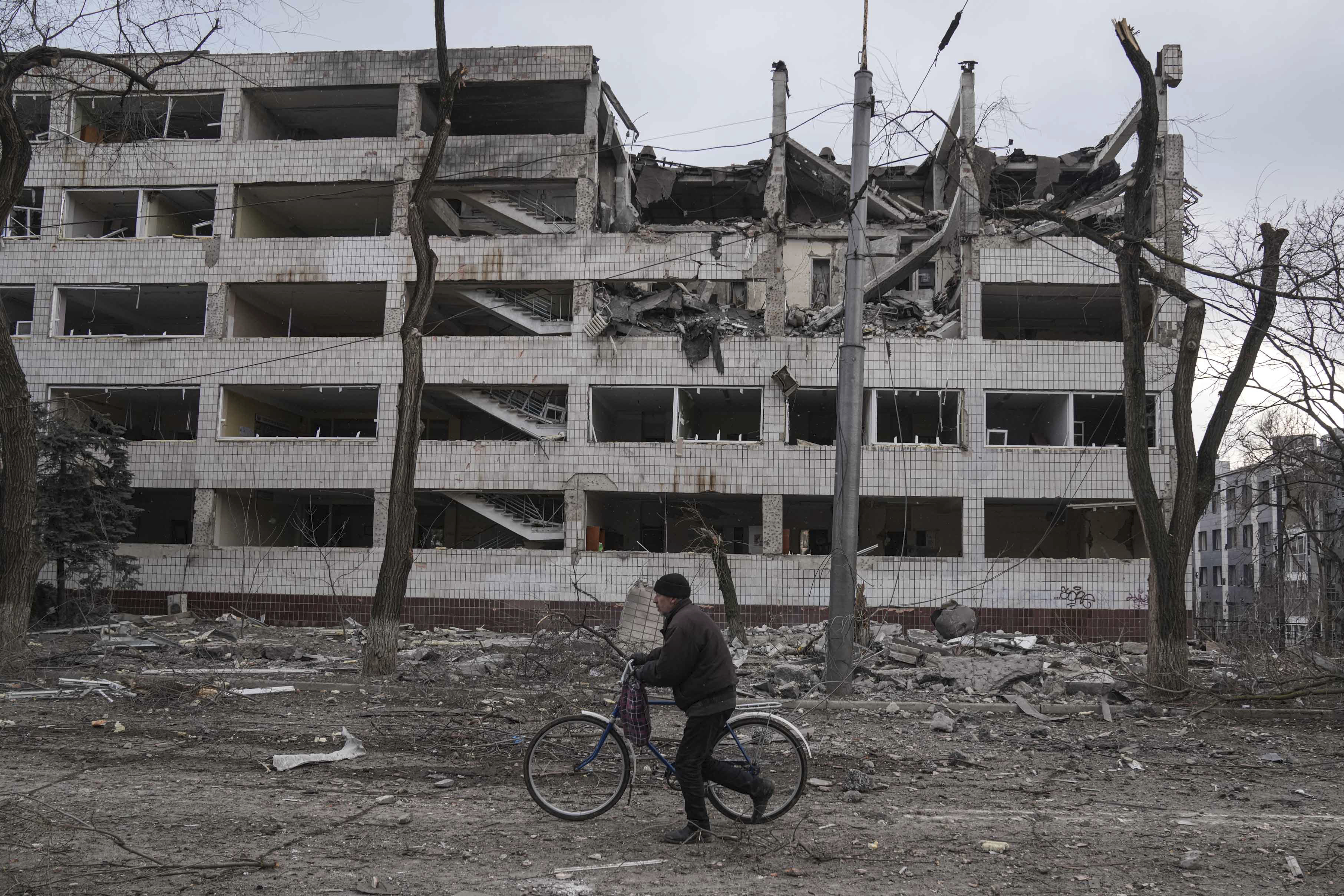 A man walks with a bicycle in front of a damaged by shelling in Mariupol, Ukraine, Thursday, March 10, 2022. (AP Photo/Evgeniy Maloletka)