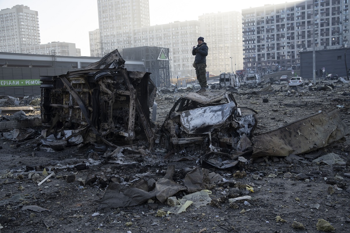 Un hombre se para sobre un automóvil destruido en medio de la destrucción causada después del bombardeo de un centro comercial, en Kiev, Ucrania (AP Photo/Rodrigo Abd)