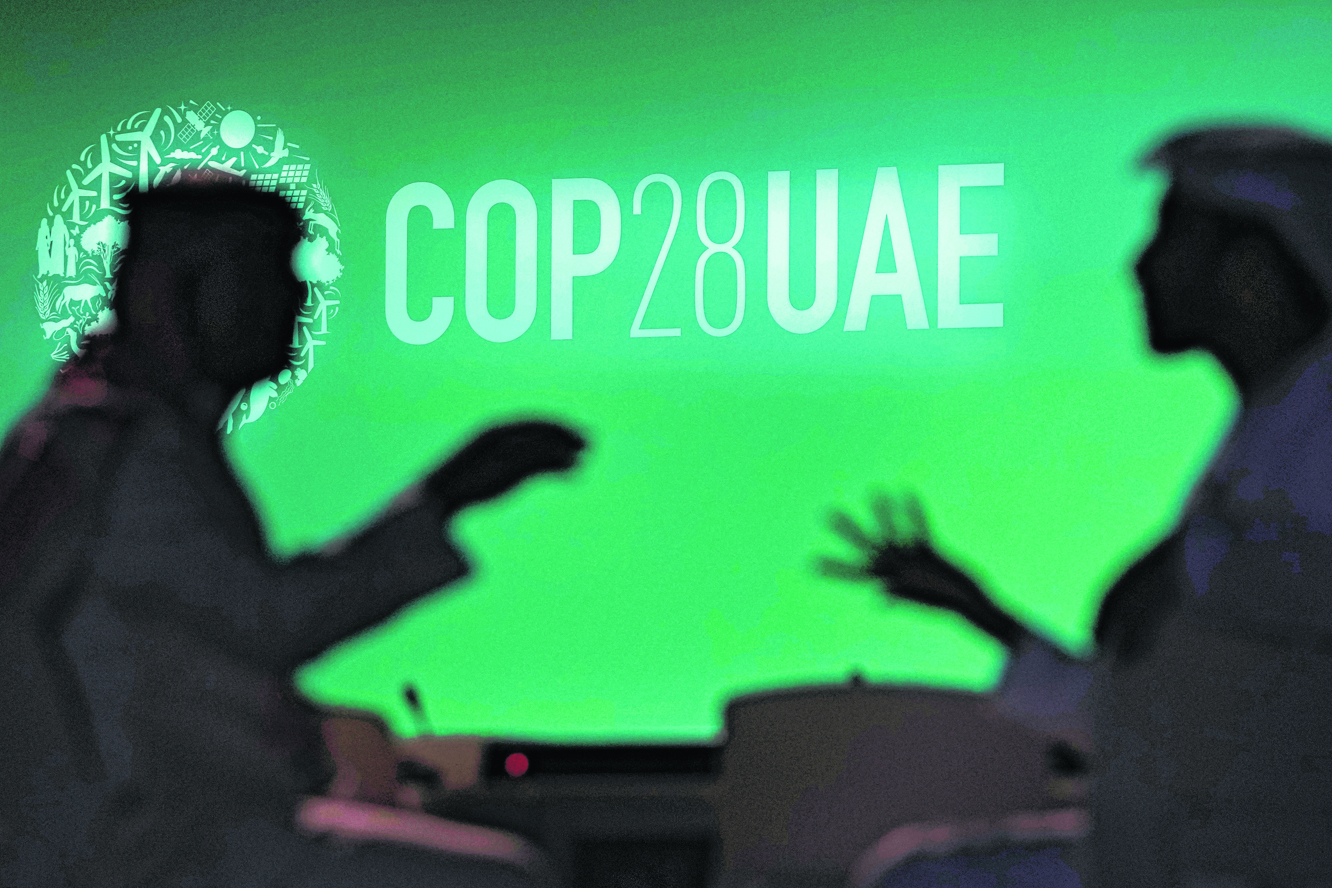 FILE - People are silhouetted against a logo for the COP28 U.N. Climate Summit, Nov. 29, 2023, in Dubai, United Arab Emirates. (AP Photo/Rafiq Maqbool, File)